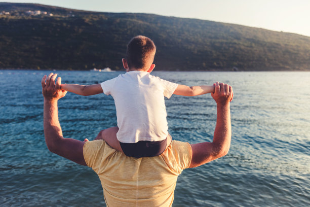 父亲和儿子在日落海滩上。爸爸和儿子在夏日的沙滩上一起玩耍。图片下载