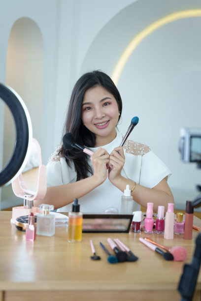 网上交易业务，一个美丽的年轻女子独立在家通过摄像头向顾客审查化妆品产品，增加他们做出购买决定的兴趣图片下载