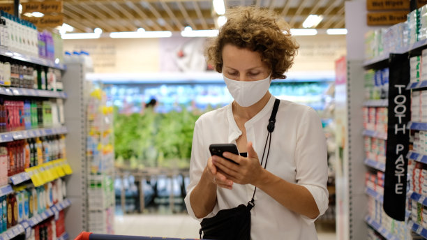 女顾客在超市非食品部购物时，一边用智能手机发短信，一边在在线应用程序中查看购物清单。新技术在营销中的应用。图片下载