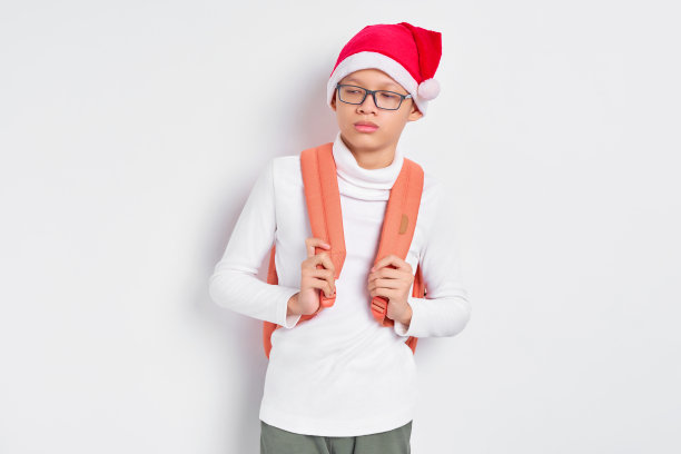 困惑英俊年轻的亚洲学生，戴着圣诞帽，穿着一件t恤，背包孤立在白色背景上图片下载