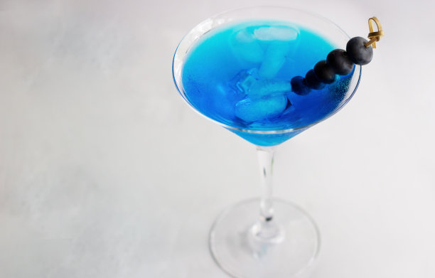 特写蓝色鸡尾酒在马提尼杯与冰块和蓝莓图片下载