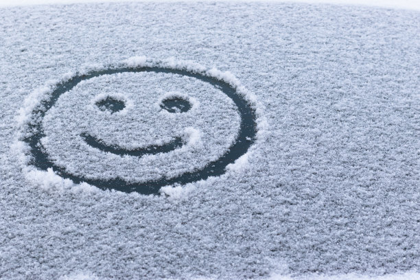 在一个阳光明媚的冬日，在被雪覆盖的汽车后窗上画一张笑脸。有选择性的重点。图片下载
