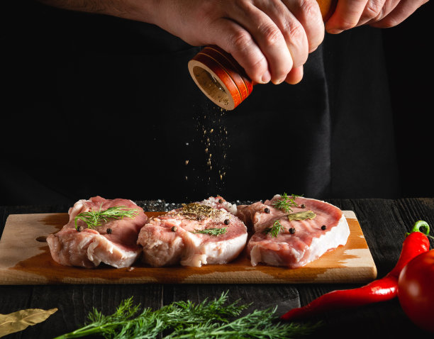 肉店厨师烹饪肉片，加入盐，胡椒和辣椒腌制黑色背景。在餐厅或咖啡馆的厨房工作环境图片下载