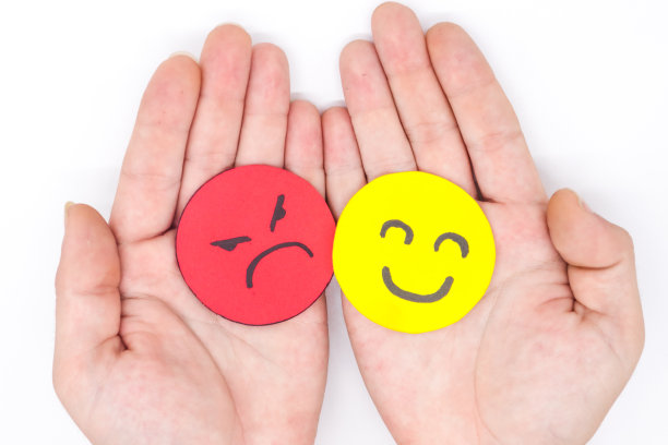 双手握着白底黄纸和红纸上的两张愤怒和快乐的脸。嫉妒，打架，愤怒，社会问题，逃避问题图片下载