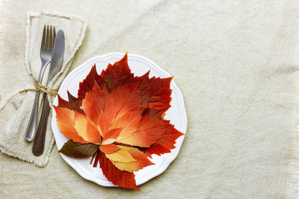 秋季餐桌摆设，亚麻餐巾、盘、刀、叉放在桌布上。顶视图白色盘子装饰秋天红叶和餐具。秋天的家居和餐桌装饰。季节性假日自然装饰图片下载
