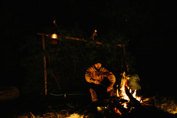 旅行者在夜晚的篝火旁休息。用一盏煤油灯和一堆石头围成的火为睡觉提供了树枝遮蔽的地方。图片下载