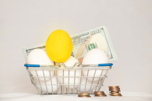 一个金色的鸡蛋和白色的鸡蛋躺在超市的篮子里，旁边是白色背景下的美元，也就是钱图片下载