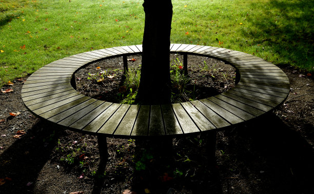 长凳四周坐着木制镶板，灰色金属板，三个座位围绕着一棵树，围绕着公园草坪上的砾石脱粒路径图片下载