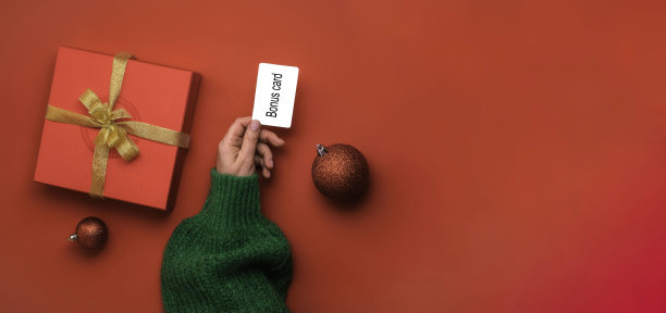 圣诞购物的概念。平躺的手穿着一件绿色毛衣，还有信用卡。红色背景的横幅图片下载