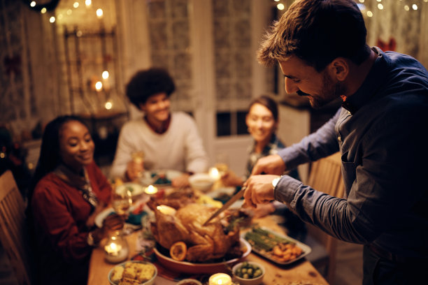 微笑的男人在餐厅用餐时雕刻感恩节火鸡。图片下载