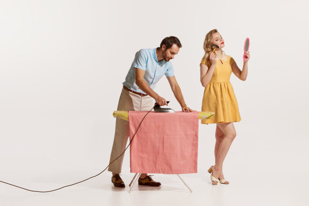 男人正在熨衣服，而美丽的女人正在化妆的肖像被隔离在白色的背景上。户主图片下载