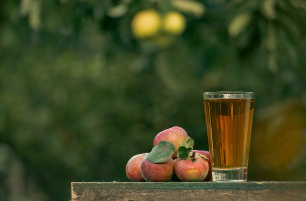 苹果汁放在花园里的木桌上，桌子周围都是苹果。农夫拿着一个罐子，把苹果园里的新鲜果汁倒进玻璃杯里。把苹果汁倒进玻璃杯里图片下载