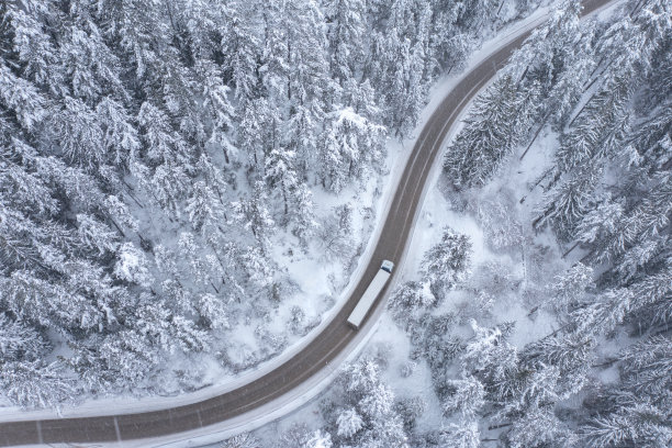 雪天卡车行驶在蜿蜒的山路上，穿过雪林图片下载