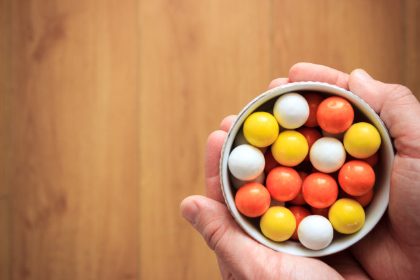 俯视图彩色糖果在白色碗在男人的手上与复制空间。图片下载