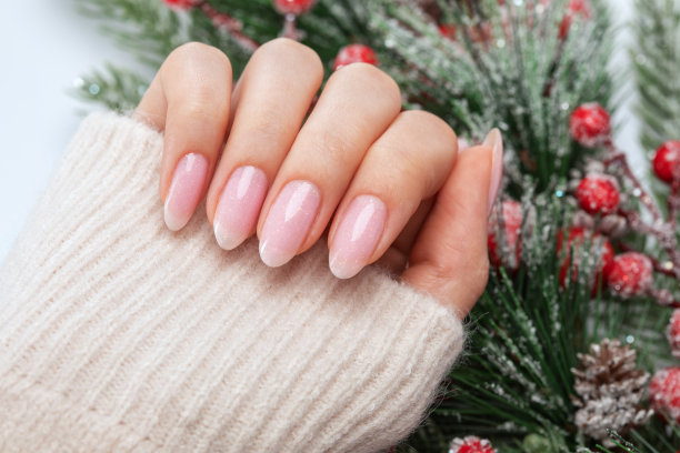 女人的手有美丽的淡粉色美甲。女孩拿着一根圣诞树树枝。专业护理手。新年的概念。图片下载