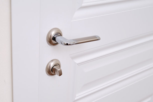 家里的房间里有一扇带锁的白色门和一个电灯开关。公寓里的金属门把手图片下载