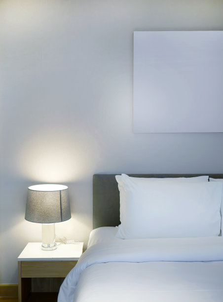 简约舒适的床上用品和时髦的台灯在现代设计的卧室，白色和灰色的色调，木地板，白色空白挂画的复制空间图片下载