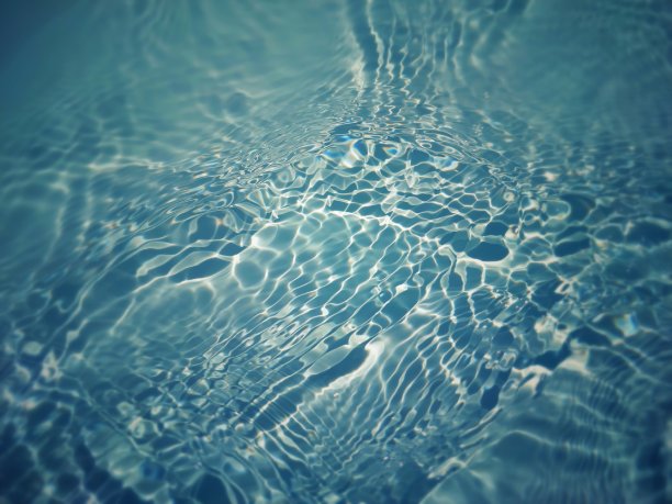 离焦模糊透明蓝色清澈平静的水面纹理与飞溅和气泡。新潮抽象的自然背景。阳光下的水波与复制空间。蓝色水彩闪亮的图片下载