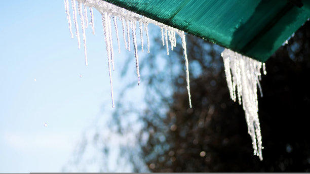 冬天，结霜，下雪，晴天。特写，巨大的透明冰柱悬挂在屋顶上，对着天空。图片下载