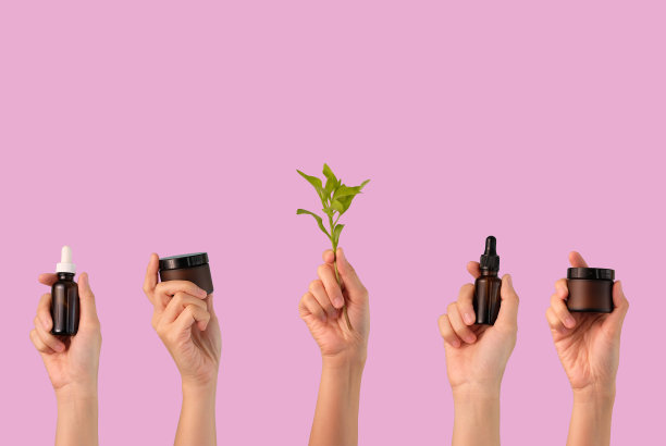 手持美容产品包装与绿叶在粉红色的背景。天然美容有机护肤有机护肤。图片下载