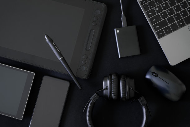 触控笔和图形平板，黑色背景屏幕，旁边是耳机，笔记本电脑，电脑鼠标，外部ssd驱动器和移动设备。现代小玩意的创意概念。图片下载