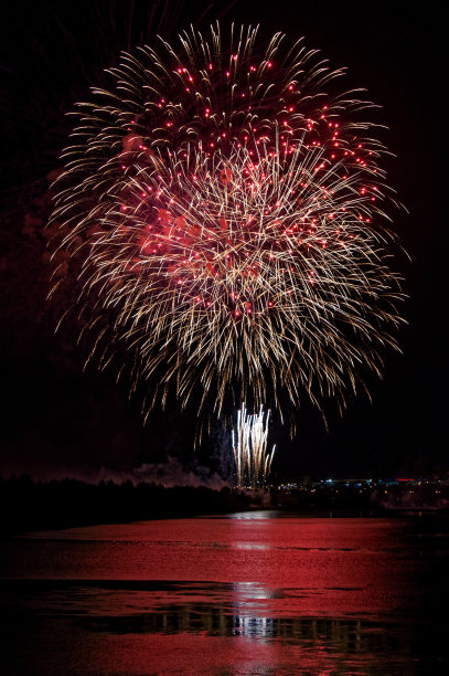 巨大的彩色烟花在城市的湖边或河岸上，带有红色、粉色和白色的条纹。倒影在水里。晚上的节日。图片下载