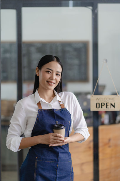 年轻的亚裔女员工站在店门口，店门口有一个开餐饮概念店的牌子。图片下载