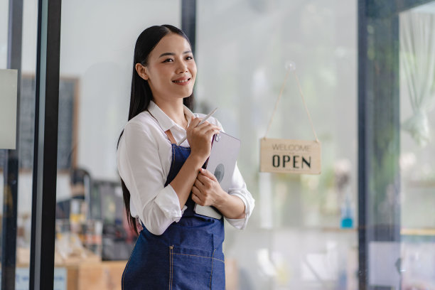 年轻的亚裔女员工站在店门口，店门口有一个开餐饮概念店的牌子。图片下载