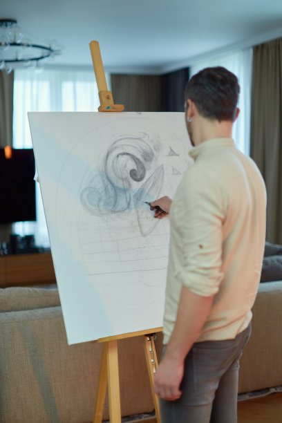 时尚的创意男子绘画在画架，后视图。艺术家在家里用铅笔写生。创造力、灵感、艺术图片下载