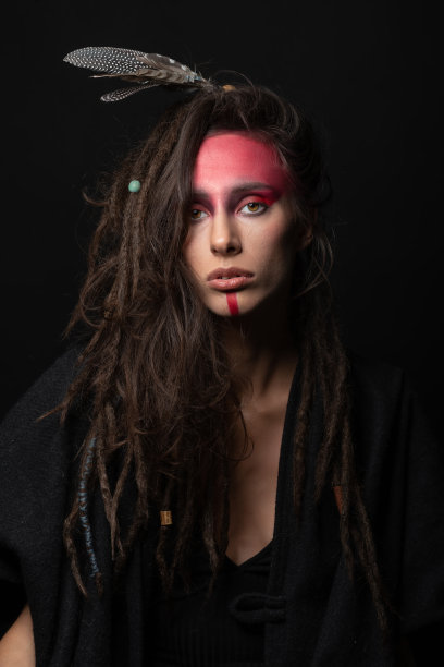 工作室肖像的女人与红色印第安部落化妆，脏辫和羽毛的头发图片下载
