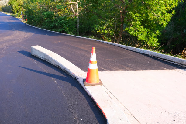 橙色道路施工安全交通锥在新鲜的黑色沥青表面进行道路修复施工养护工作期间，在人行道路边城市街景照片图片下载