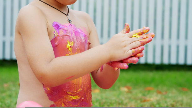 一个小孩，一个四岁的男孩在玩，用手指画画画，装饰自己，在花园里，坐在毯子上，在草地上，在夏天。他很开心图片下载