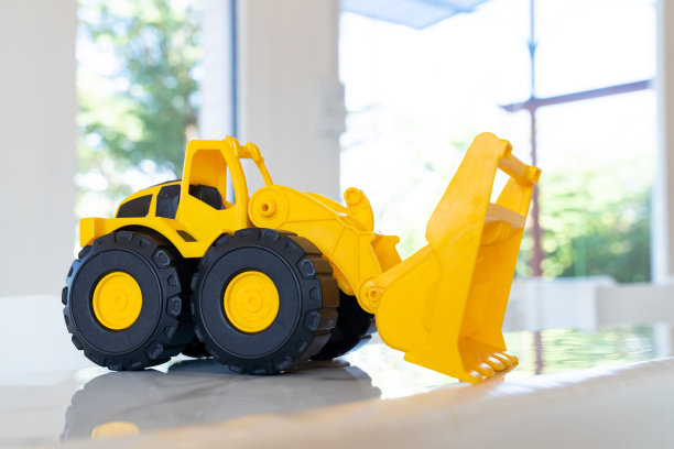一张桌子上放着一辆黄色的装载机玩具车，上面有结实的塑料制成的铰接部件。图片下载
