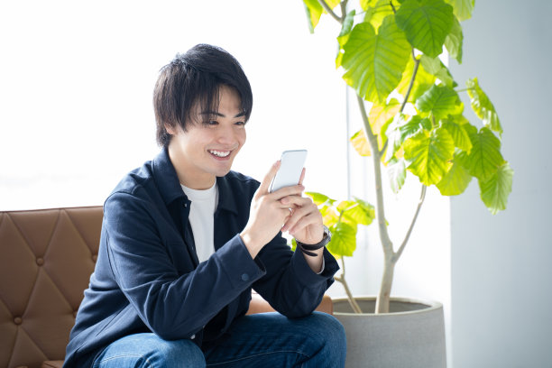 一个开着智能手机的20多岁的男人坐在客厅的沙发上放松图片下载