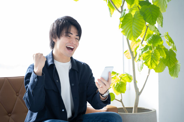 一个20多岁的男人看着他的智能手机，摆出一个大胆的姿势——在客厅的沙发上放松图片下载