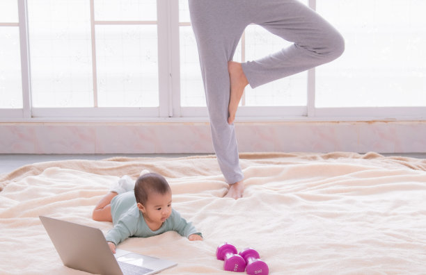 亚洲妈妈分娩后锻炼，年轻妈妈看视频训练减肥瑜伽运动的电脑笔记本电脑，美丽的女人和蹒跚学步的婴儿一起玩爱和照顾图片下载
