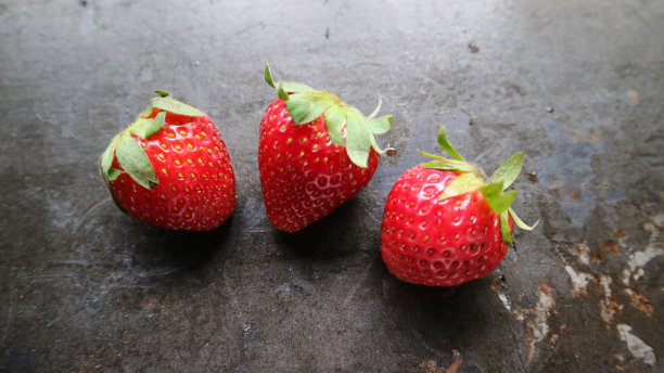 三个成熟的浆果红色草莓在黑色木桌背景。宏。水平的照片图片下载