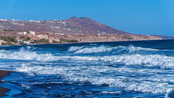 在希腊圣托里尼岛，波涛起伏的爱琴海以岩石山为背景的风景照片图片下载