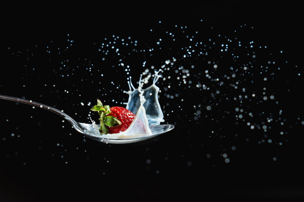 特写镜头草莓放在勺子上，水溅在黑色背景上图片下载