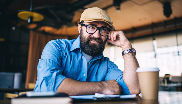 快乐繁荣的男性作家在眼镜视力矫正享受自由时间在咖啡馆内部，微笑胡须成熟的男人满足于休闲和咖啡休息梦想的想法和计划图片下载