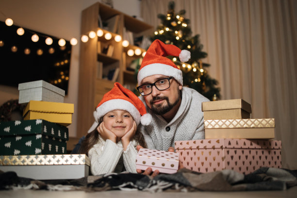 留着大胡子的年轻白人父亲躺在地板上，带着他可爱的学龄前女儿和礼物图片下载