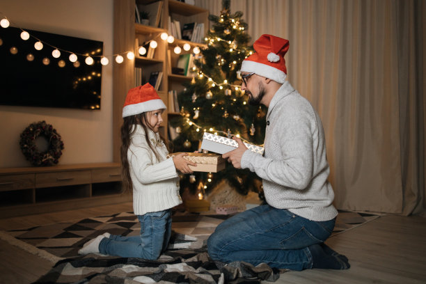 圣诞节的家庭庆祝活动。微笑的年轻男子与他可爱的女儿交换分享圣诞礼物图片下载