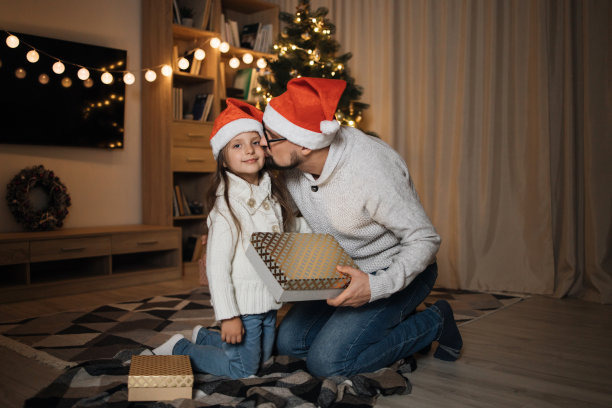 有吸引力的白人男性分享礼物和亲吻他可爱的学龄前女儿在圣诞老人的帽子图片下载