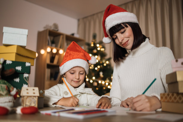 年轻美丽的母亲和可爱的小女儿戴着红帽子给圣诞老人写信图片下载