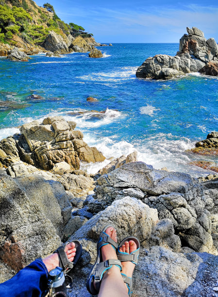 岩石海岸的全景照片与游客的脚凉鞋，女人和男人。让普通人沿着海岸徒步旅行的概念。图片下载