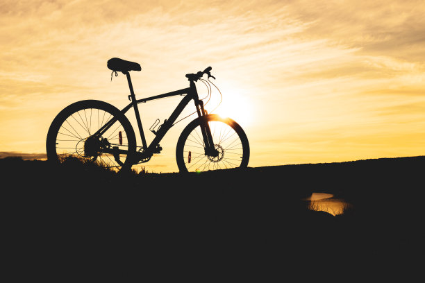 自行车剪影在山上靠近河流，橙色的日落天空和模糊的云图片下载