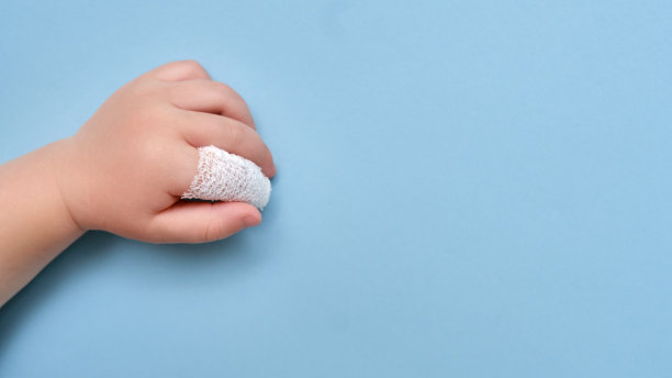 婴儿的手与绷带的手指在工作室蓝色的背景，复制空间。儿童食指受伤，用白色绷带包扎图片下载