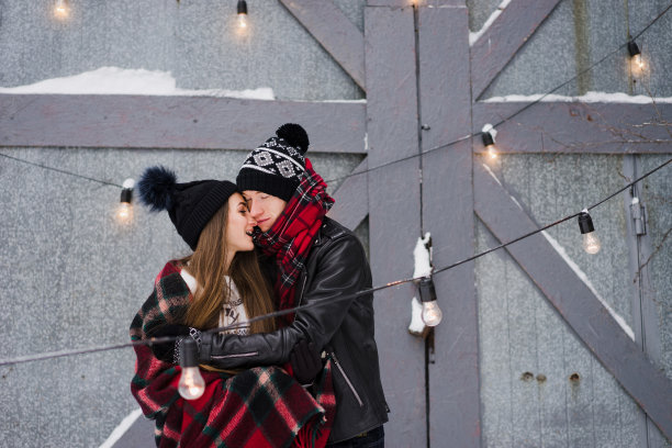 欢快的情侣穿着温暖舒适的衣服，在花园里用彩色的毯子拥抱取暖。图片下载