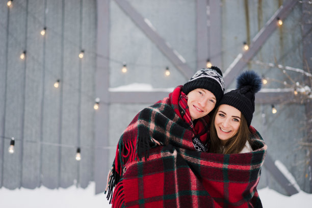 欢快的情侣穿着温暖舒适的衣服，在花园里用彩色的毯子拥抱取暖。图片下载