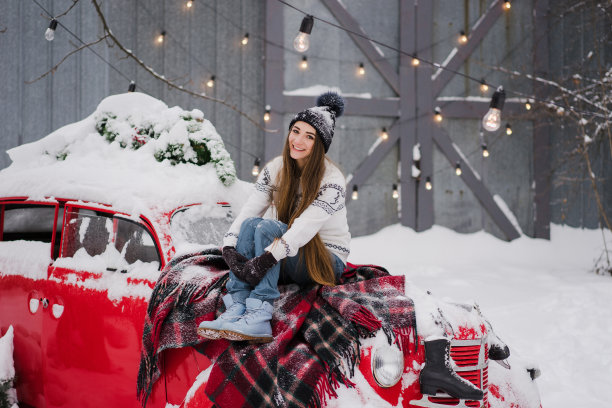 美丽的女人穿着温暖舒适的衣服坐在一辆覆盖着雪的红色老爷车上。图片下载